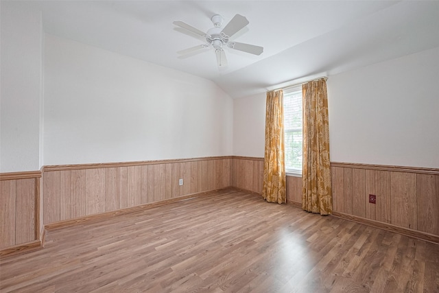 unfurnished room with wooden walls, a wainscoted wall, a ceiling fan, wood finished floors, and vaulted ceiling
