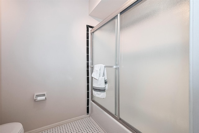 bathroom with baseboards, combined bath / shower with glass door, and toilet