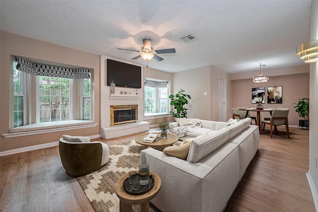 living area with baseboards, a ceiling fan, wood finished floors, and visible vents