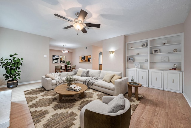 living room featuring ceiling fan, visible vents, arched walkways, baseboards, and light wood-style floors