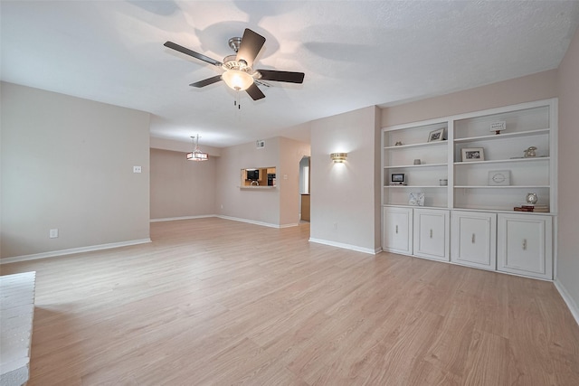 unfurnished living room with arched walkways, light wood-style flooring, a ceiling fan, baseboards, and visible vents