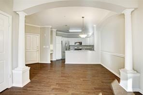 unfurnished living room with ornate columns, arched walkways, dark wood finished floors, and baseboards