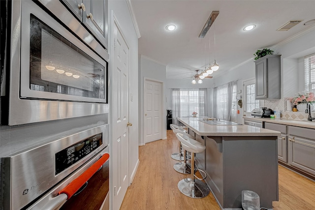 kitchen with appliances with stainless steel finishes, crown molding, gray cabinetry, a center island, and light wood-type flooring