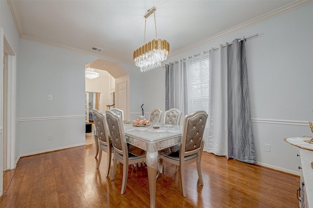 dining space featuring arched walkways, ornamental molding, wood finished floors, a chandelier, and baseboards