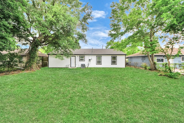 back of property with central AC, fence, and a yard