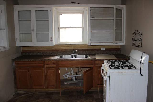kitchen featuring brown cabinets, dark countertops, a sink, white gas range, and glass insert cabinets