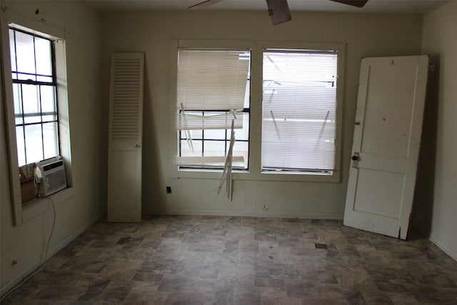 spare room featuring baseboards, ceiling fan, stone finish flooring, and a wealth of natural light