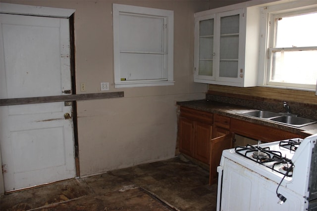 kitchen with brown cabinetry, a sink, white gas stove, and glass insert cabinets