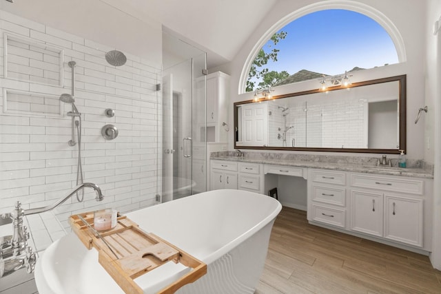 bathroom with double vanity, a freestanding tub, a shower stall, and wood finished floors