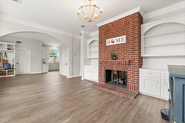 unfurnished living room with crown molding, a brick fireplace, arched walkways, light wood finished floors, and a notable chandelier