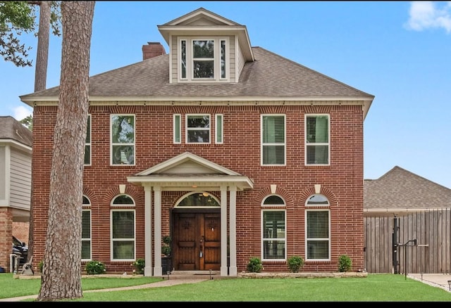 view of front of home featuring a shingled roof, a front lawn, and brick siding