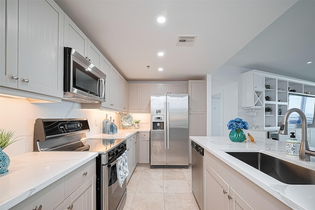 kitchen with appliances with stainless steel finishes, a sink, visible vents, and light stone counters