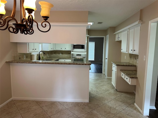 kitchen with a peninsula, dark stone counters, a sink, a notable chandelier, and stainless steel appliances