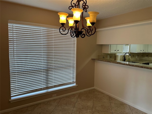 kitchen featuring hanging light fixtures, a sink, light tile patterned floors, baseboards, and a chandelier