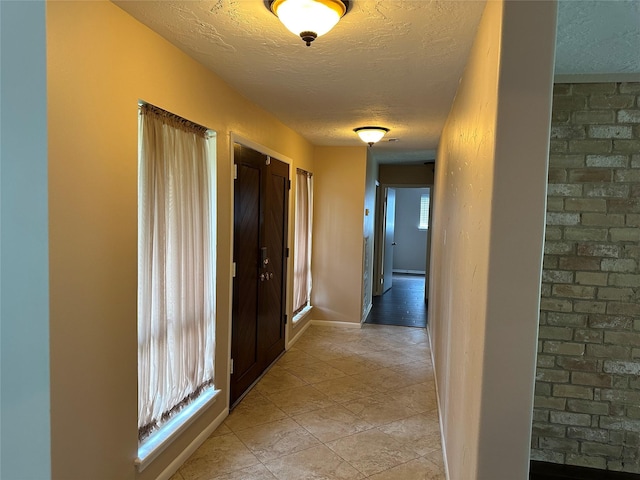 hall with light tile patterned floors, a textured ceiling, a healthy amount of sunlight, and baseboards