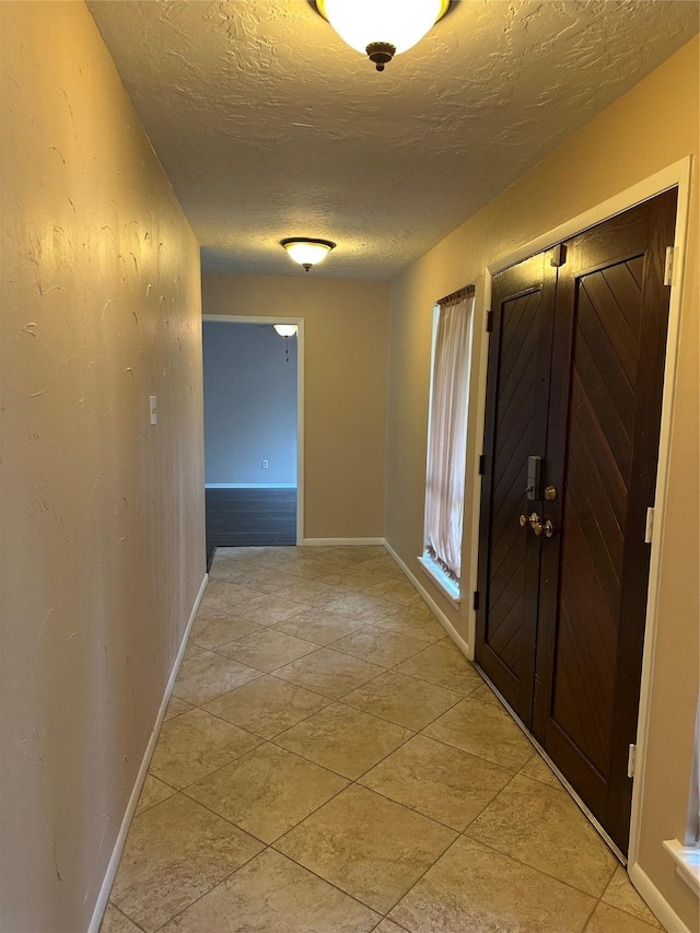 hallway featuring a textured ceiling and baseboards