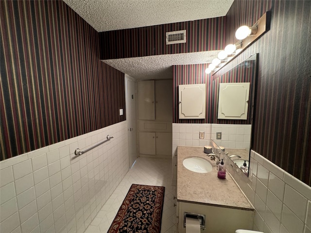bathroom featuring wallpapered walls, a textured ceiling, vanity, and tile walls
