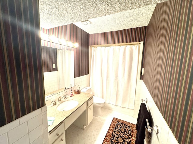full bathroom featuring wainscoting, vanity, toilet, a textured ceiling, and wallpapered walls