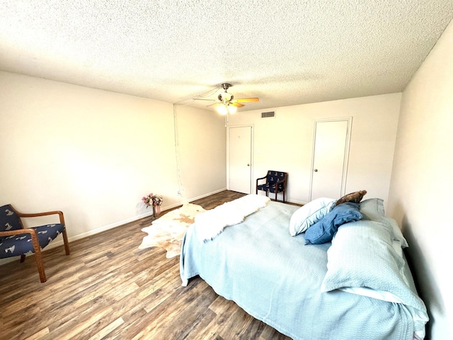 bedroom with a ceiling fan, a textured ceiling, visible vents, and wood finished floors