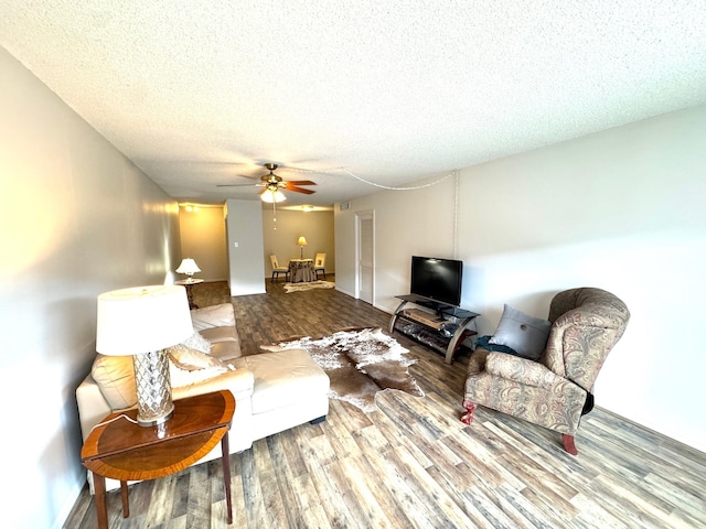 living room with a textured ceiling, ceiling fan, and wood finished floors