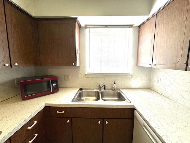 kitchen with light countertops, white dishwasher, dark brown cabinetry, and a sink