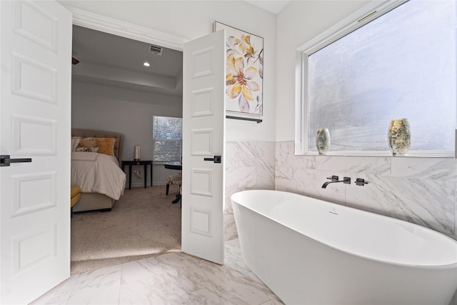 full bath with visible vents, marble finish floor, a freestanding tub, tile walls, and ensuite bathroom