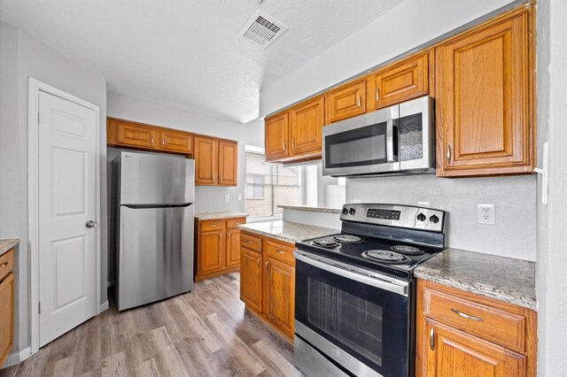 8803 Enchanted Forest Dr, Houston, TX 77088 - kitchen with visible vents, brown cabinetry, light wood-type flooring, tasteful backsplash, and appliances with stainless steel finishes