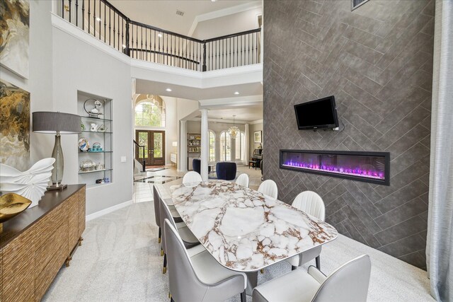 dining area with decorative columns, a towering ceiling, built in shelves, a glass covered fireplace, and carpet flooring