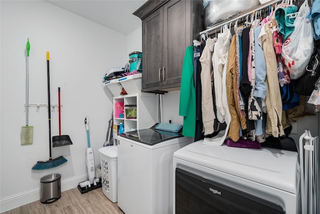 clothes washing area featuring light wood-type flooring, cabinet space, baseboards, and washing machine and clothes dryer