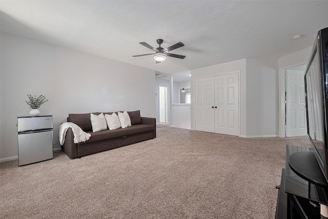 carpeted living area with baseboards and ceiling fan
