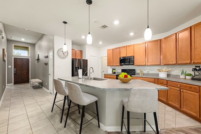 kitchen with backsplash, visible vents, black electric range, a sink, and stainless steel fridge