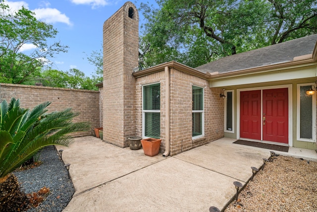 doorway to property with brick siding, a shingled roof, fence, and a chimney