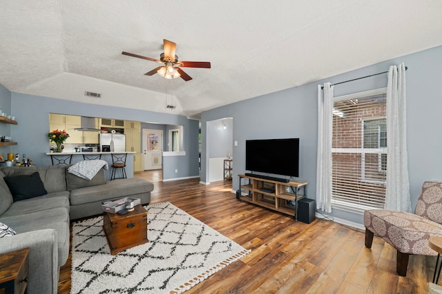 living area with a textured ceiling, ceiling fan, wood finished floors, and a tray ceiling