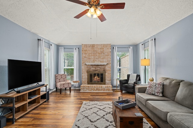 living room with hardwood / wood-style floors, ceiling fan, a brick fireplace, and a textured ceiling