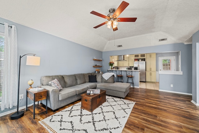living area featuring visible vents, lofted ceiling, wood finished floors, a textured ceiling, and a ceiling fan