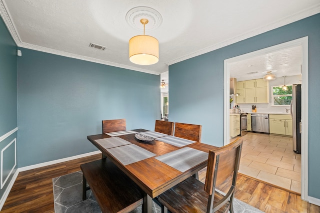 dining space featuring crown molding, baseboards, light wood finished floors, and visible vents