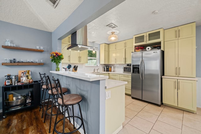 kitchen with a peninsula, a textured ceiling, cream cabinets, island exhaust hood, and stainless steel appliances