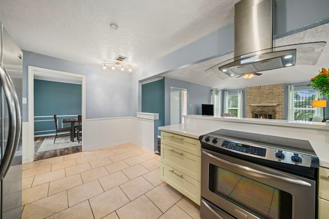 kitchen with appliances with stainless steel finishes, light countertops, extractor fan, a wainscoted wall, and light tile patterned floors