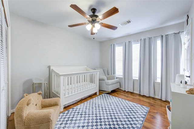 bedroom with visible vents, a crib, ceiling fan, and wood finished floors