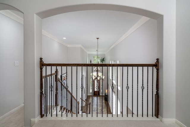 hall featuring arched walkways, baseboards, a chandelier, ornamental molding, and carpet