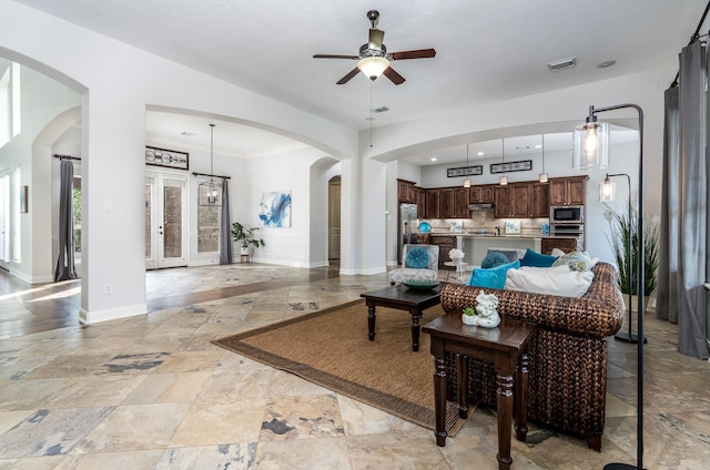 living area featuring ceiling fan, arched walkways, baseboards, visible vents, and stone tile flooring