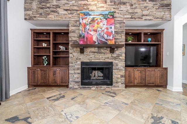 living area featuring baseboards, stone tile floors, and a stone fireplace
