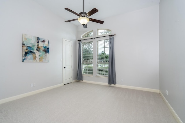 empty room featuring light colored carpet, a ceiling fan, and baseboards