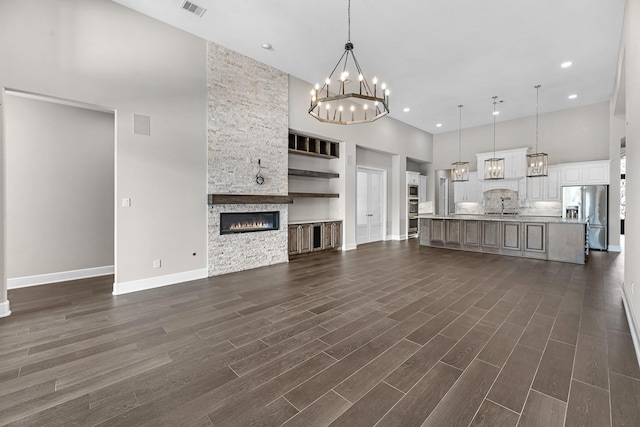 unfurnished living room featuring a towering ceiling, a fireplace, baseboards, a chandelier, and dark wood-type flooring