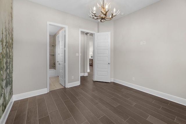 unfurnished bedroom featuring an inviting chandelier, dark wood finished floors, ensuite bathroom, and baseboards
