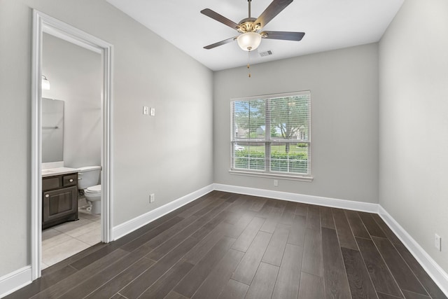 unfurnished bedroom with ceiling fan, visible vents, baseboards, connected bathroom, and dark wood-type flooring