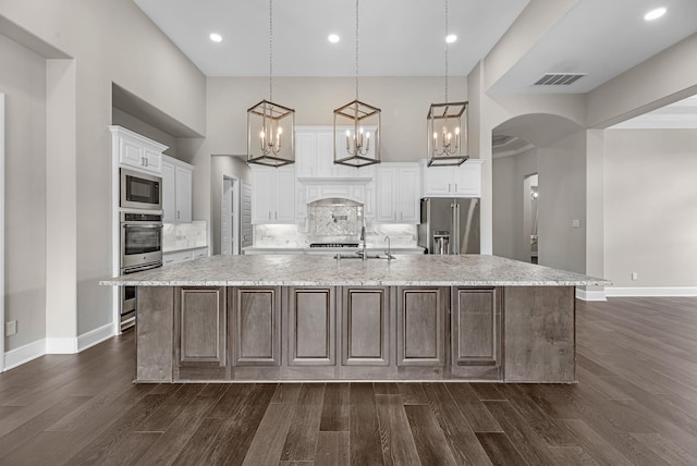 kitchen featuring visible vents, arched walkways, stainless steel appliances, a spacious island, and dark wood-style floors