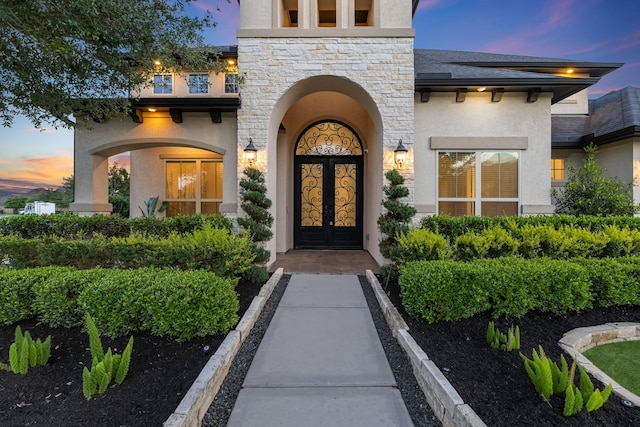 exterior entry at dusk featuring stucco siding and stone siding