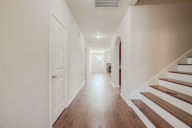 hall featuring visible vents, stairs, wood finished floors, baseboards, and arched walkways