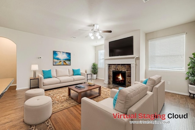 living area featuring arched walkways, ceiling fan, a fireplace, and wood finished floors